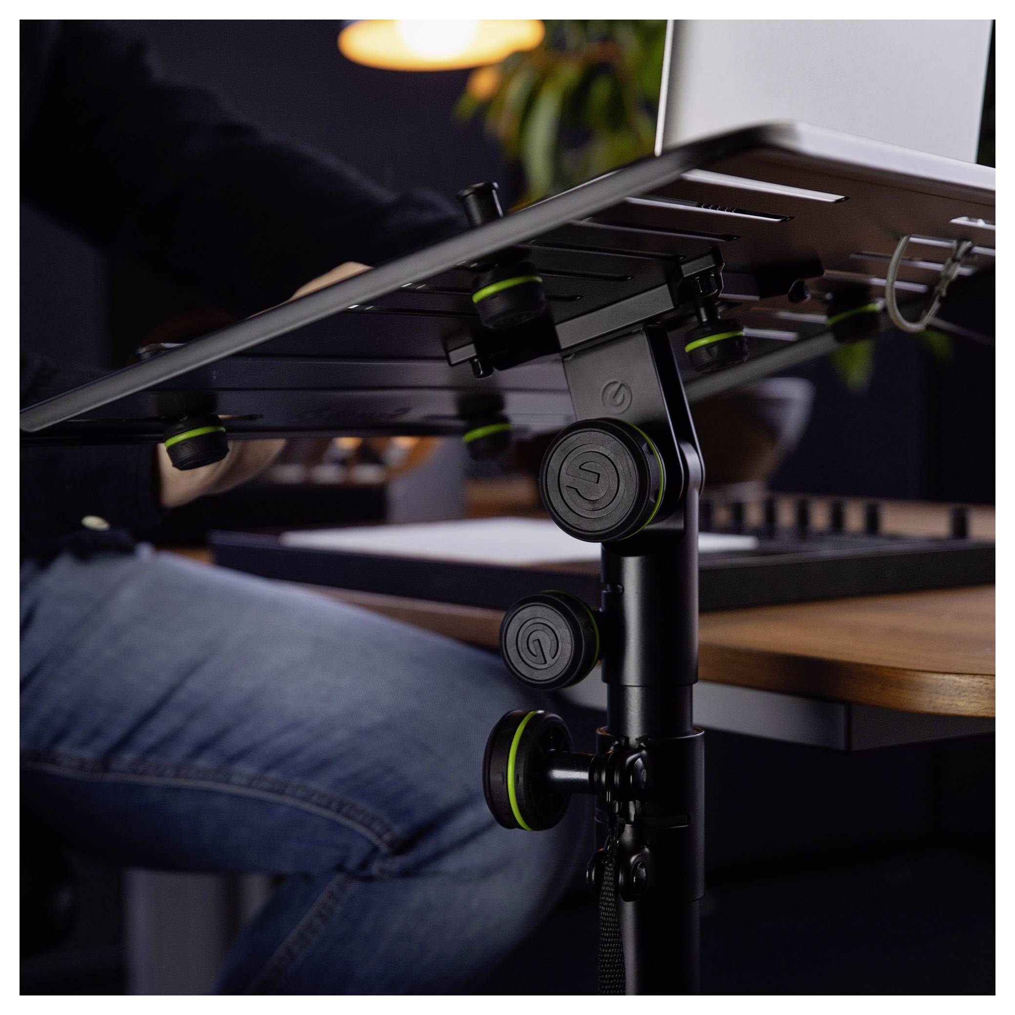 Nahaufnahme einer verstellbaren schwarzen Schreibtischhalterung, die einen Monitor neben einer sitzenden Person an einem Holzschreibtisch stützt.