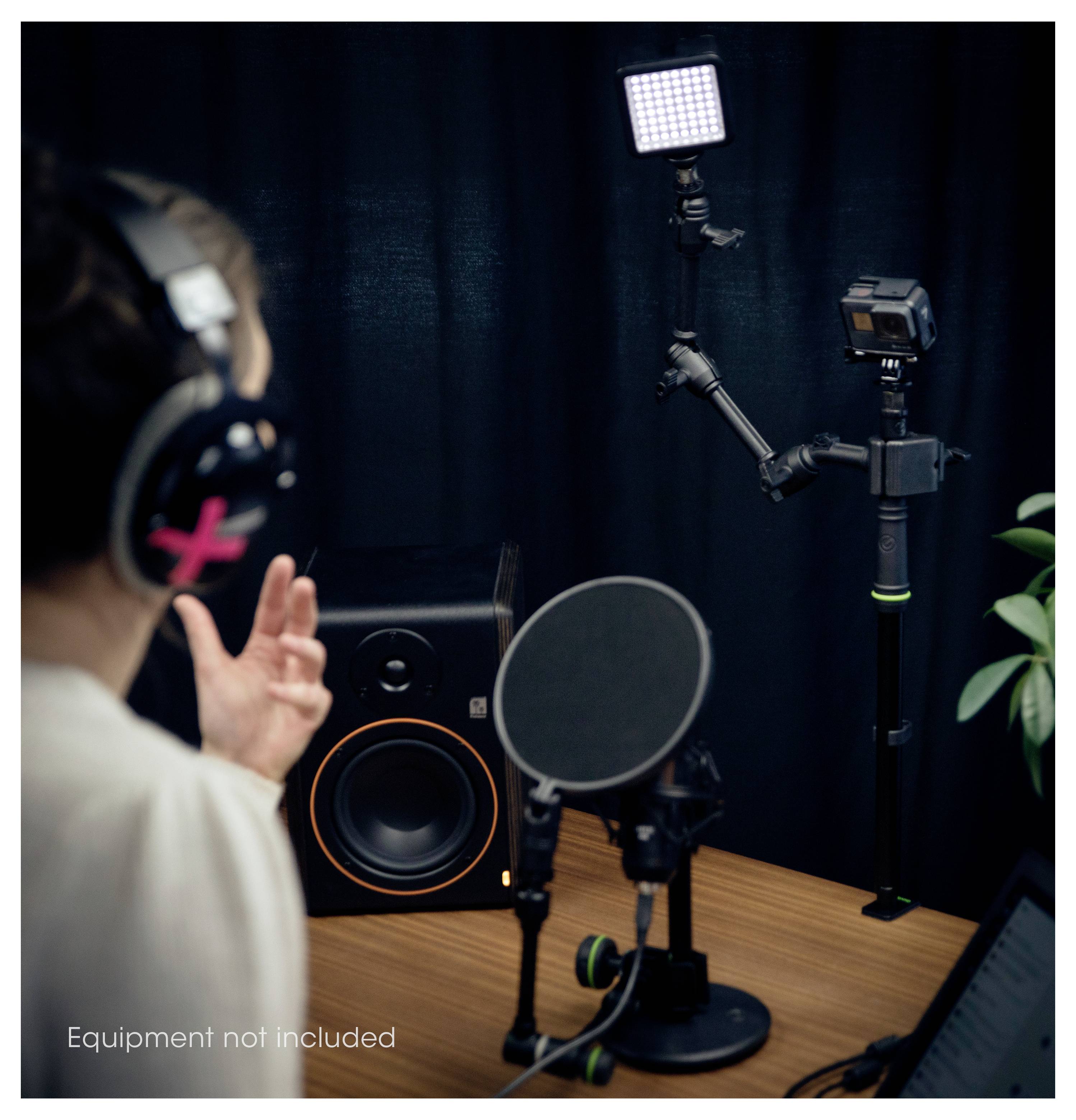 Eine Person nimmt Audio in einem Studio auf und steht dabei einem Mikrofon mit Popschutz gegenüber, umgeben von Lautsprechern, Lichtern und einer auf einem Ständer montierten Kamera.