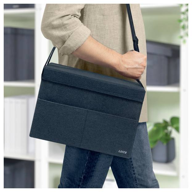 Person trägt eine dunkle Schultertasche oder einen Laptop-Koffer quer über den Körper in einer Büro- oder Wohnungsumgebung.