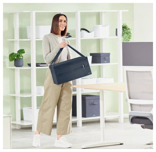 Frau in einem hellen Büro, die eine schwarze Laptoptasche neben einem Schreibtisch und Regalen hält.