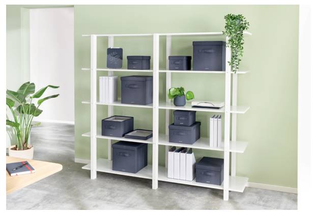 Weiße Regale mit grauen Aufbewahrungsboxen, Büchern und Pflanzen an einer hellgrünen Wand in einem hellen Raum.