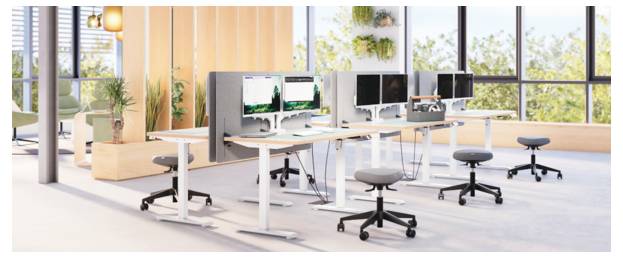 Modernes Großraumbüro mit Stehschreibtischen, Computern und Hockern in der Nähe großer Fenster und Innenbegrünung.