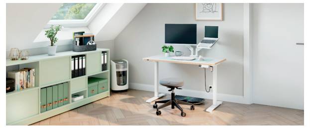 Homeoffice mit einem Schreibtisch, Computermonitor und Laptop, Drehstuhl, Aktenschrank, Pflanze und Büchern unter einer schrägen Decke.