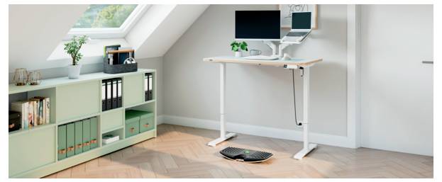 Homeoffice-Ecke mit einem Stehschreibtisch, Monitor und Laptop, einem Schrank zur Aufbewahrung und einer Tastatur auf dem Boden unter dem Schreibtisch.