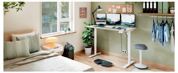 Ein kleines Schlafzimmer, das als Homeoffice eingerichtet ist, mit einem Bett neben einem Stehschreibtisch, zwei Monitoren, Stuhl, Lampe, Pflanze und Fenster.