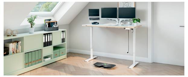 Ein Homeoffice mit einem weißen Stehschreibtisch, zwei Monitoren, einer Tastatur und einem grünen Schrank unter einem schrägen Dachfenster.