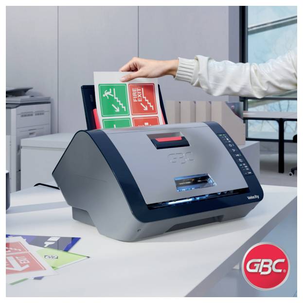 Eine Person führt ein Notausgangsschild in ein GBC-Laminiergerät auf einem Schreibtisch in einer Büroumgebung ein.