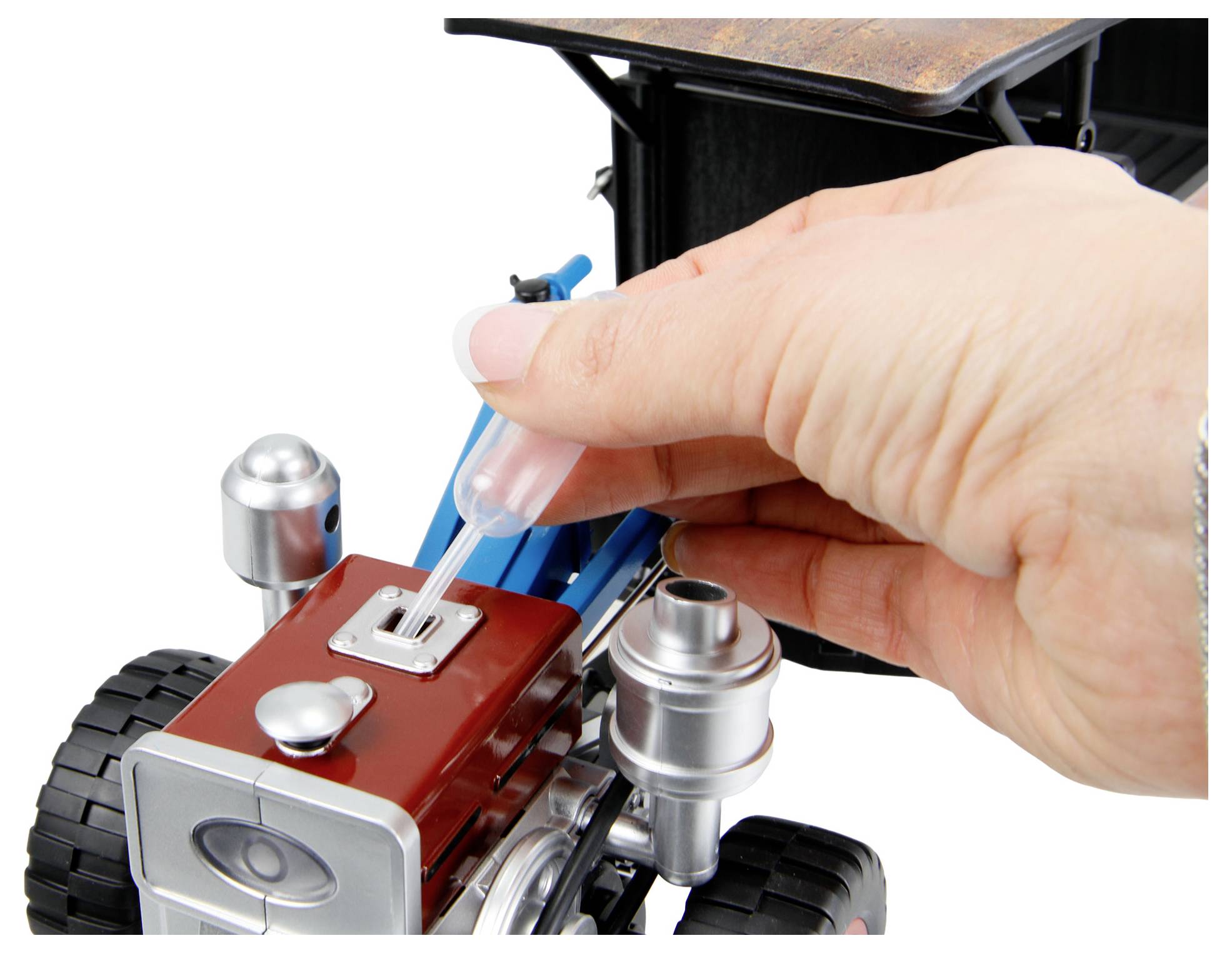 Hand, die ein klares Fläschchen in einen kleinen Spiel-Laborroboter oder ein Fahrzeug mit Rädern und Metallkomponenten platziert.