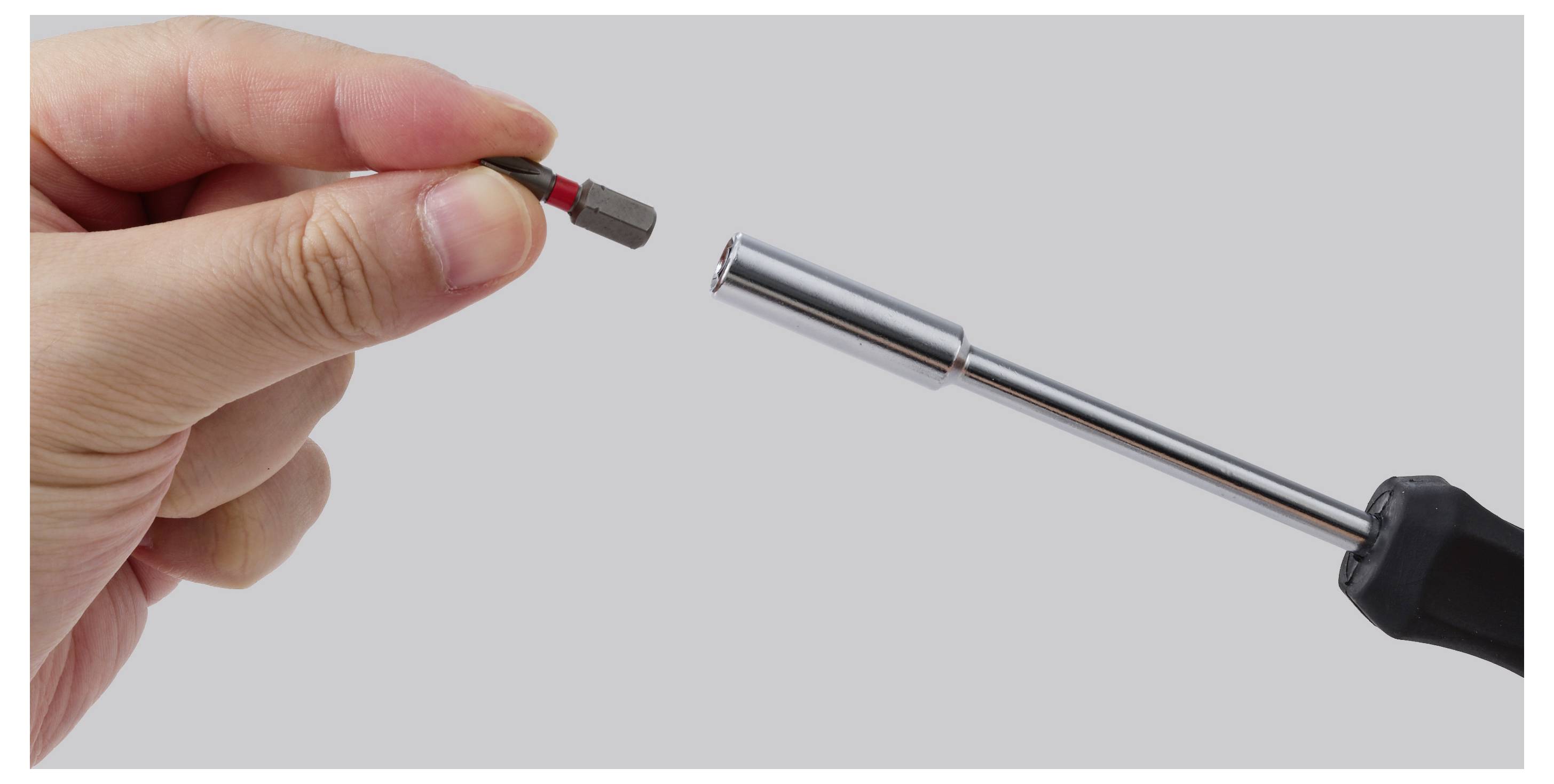 Hand, die einen kleinen Sechskantbit in einen Schraubendrehergriff gegen einen einfachen grauen Hintergrund einsetzt.