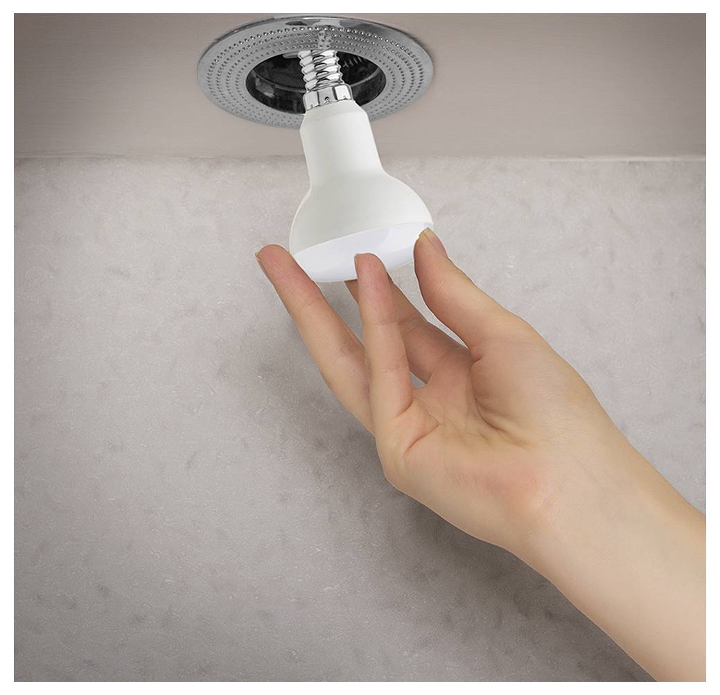 Eine Person dreht eine Glühbirne von Hand in eine Deckenleuchte gegen eine schlichte Wand.