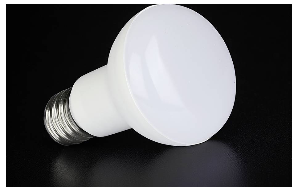 Eine weiße LED-Glühbirne liegt auf einer dunklen Oberfläche vor schwarzem Hintergrund.