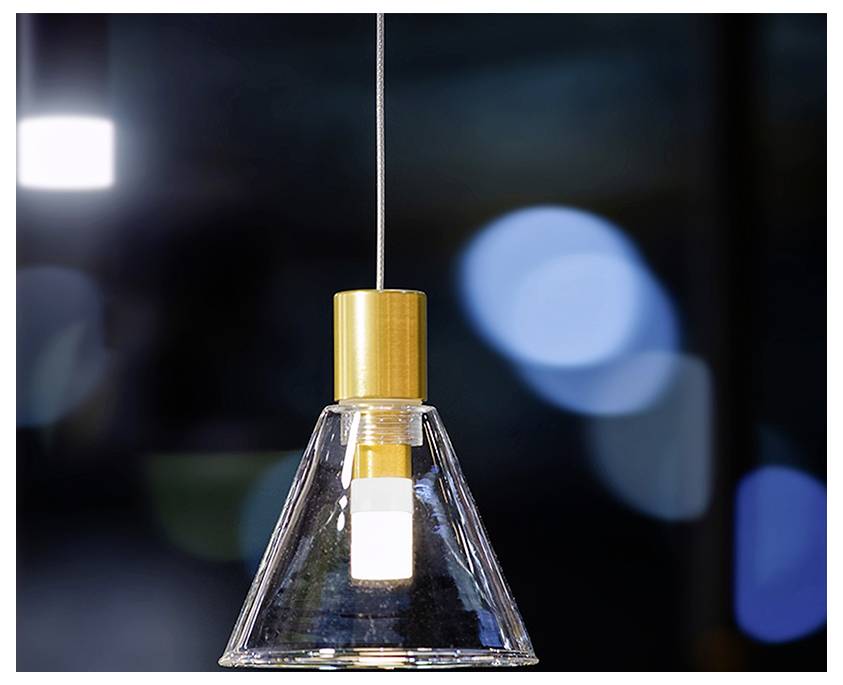 Moderne Pendelleuchte mit klarem Glaskegel-Schirm und goldenem Oberteil, hängend vor unscharfem dunklem Hintergrund.