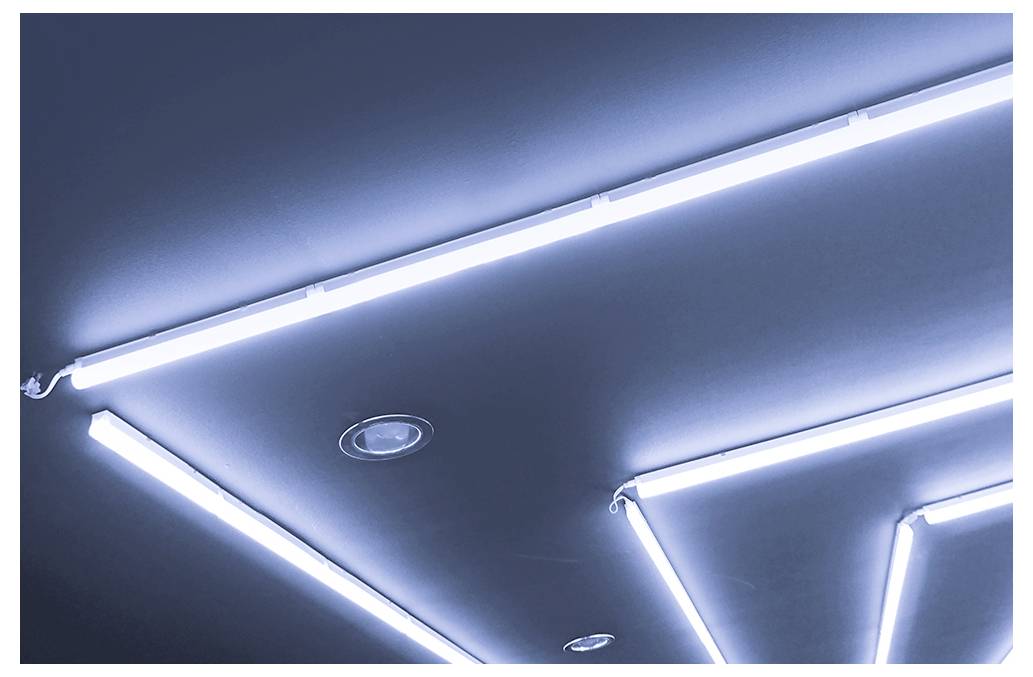 Leeres Industrielagerhaus-Interieur mit hohem Metalldach, Betonboden, hellen Deckenleuchten und einem Gabelstapler, der links hinten geparkt ist.