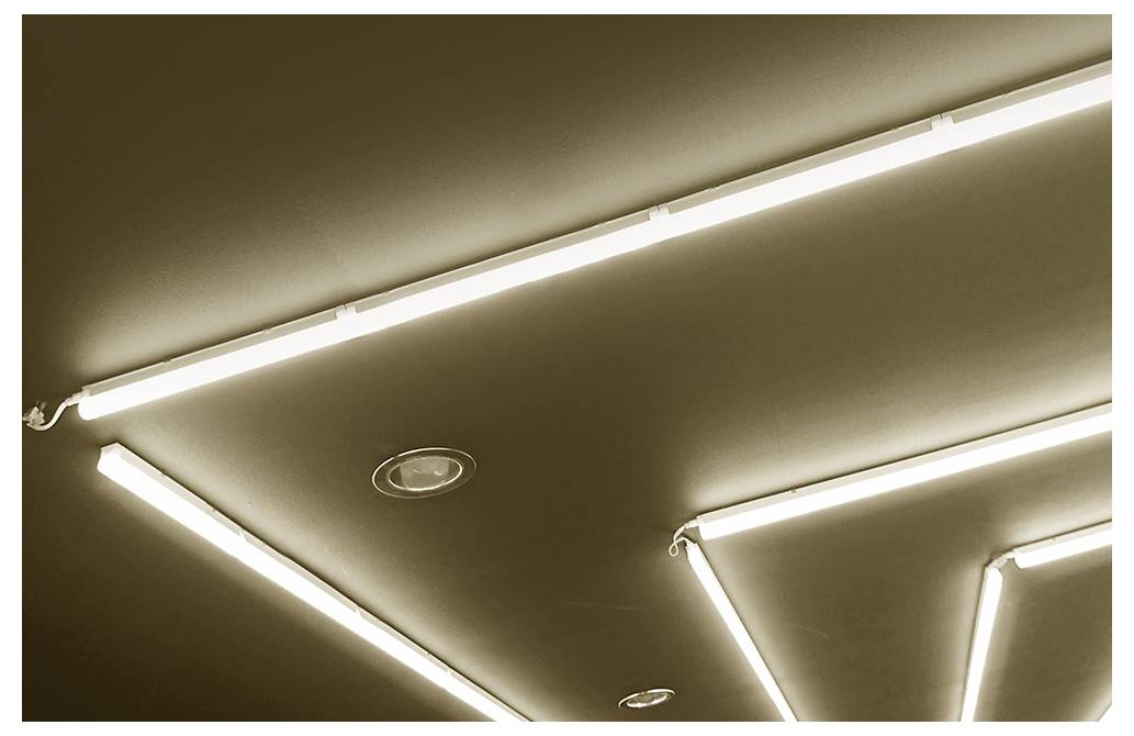 Decke mit hellen linearen Leuchtstofflampen, die in diagonalen und rechteckigen Mustern angeordnet sind.