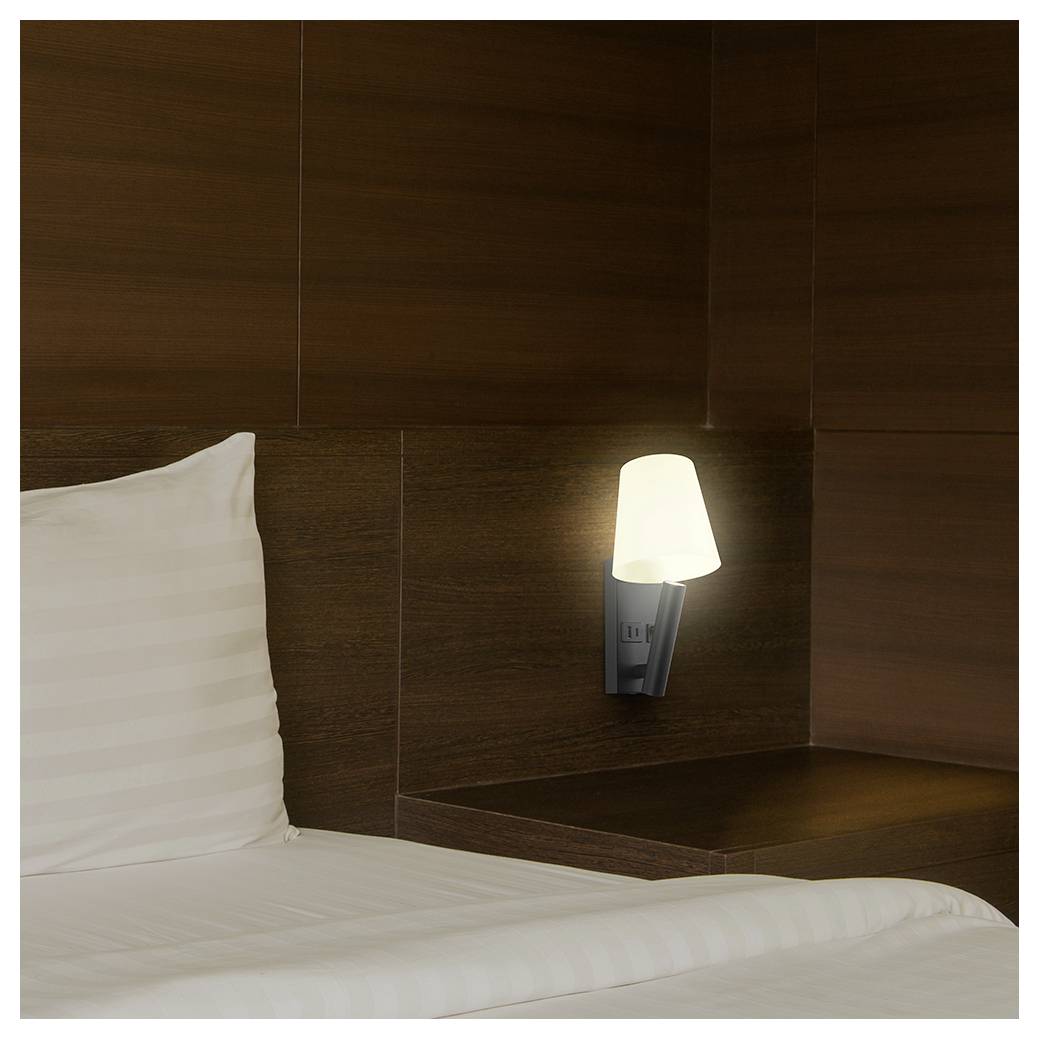 Nahaufnahme eines ordentlich gemachten Bettes mit einem weißen Kissen und einer leuchtenden Wandleuchte in einem dunkel getäfelten Schlafzimmer.