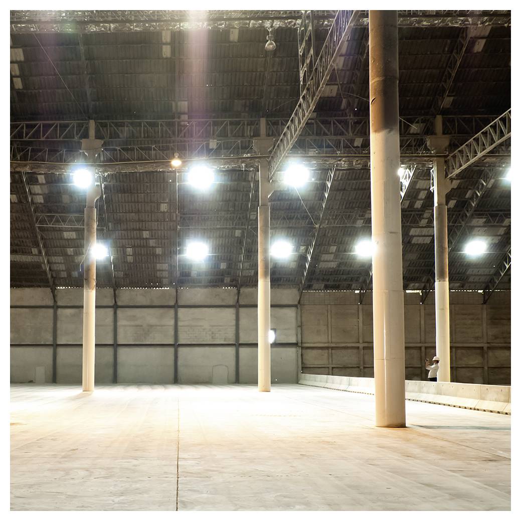 Leeres Industrielagerhausinterieur mit hohen Stützpfeilern, hellen Deckenleuchten und Betonboden
