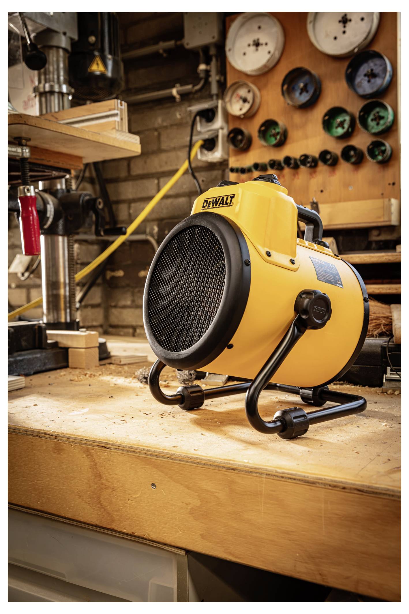 Gelber tragbarer DeWalt-Elektroheizer auf einer Werkbank in einer Werkstatt, mit Messinstrumenten und Werkzeugen im Hintergrund.