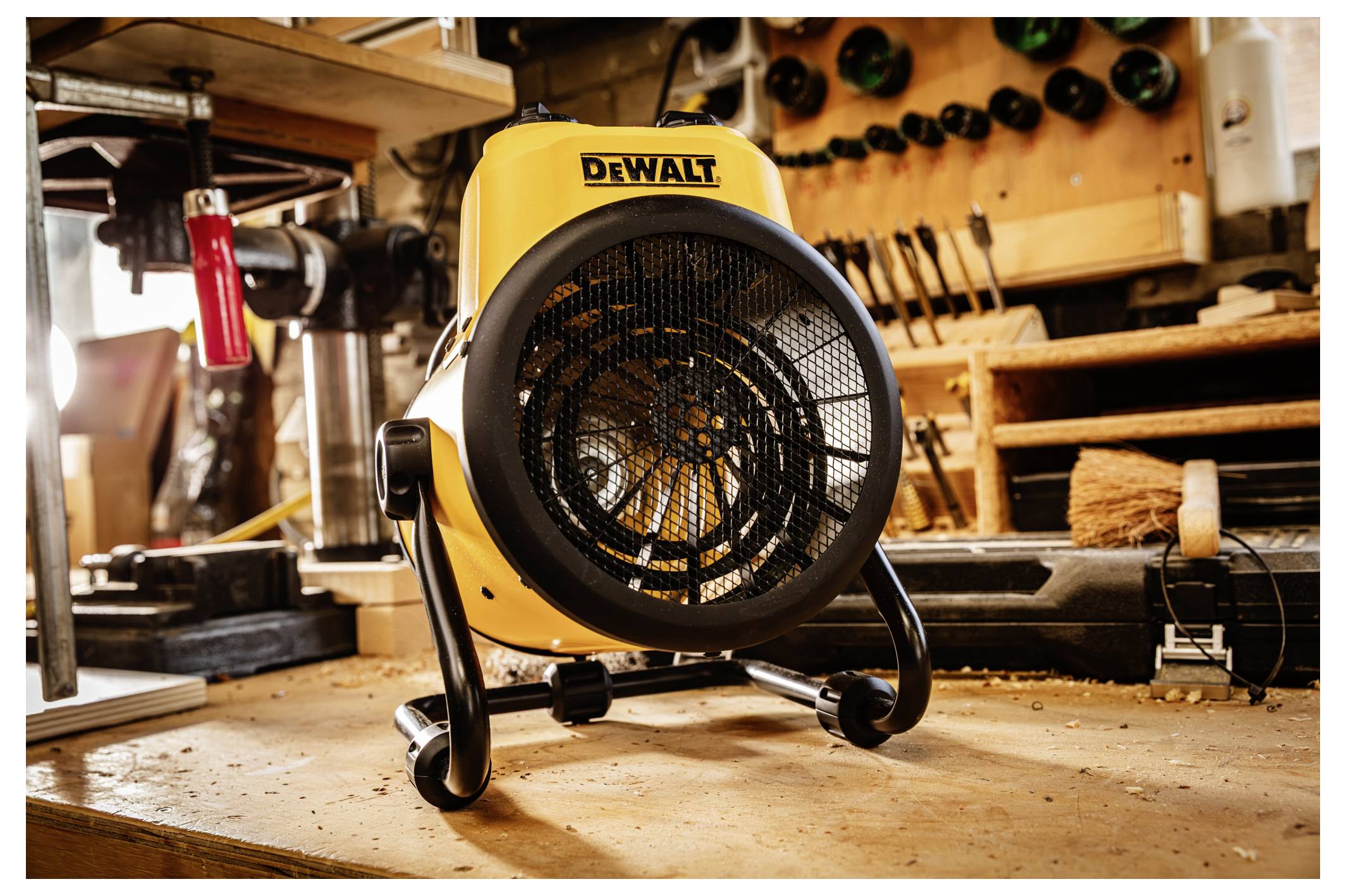 Gelber tragbarer DEWALT-Ventilator auf einem Werkstattboden, nach vorne ausgerichtet mit Werkzeugen und hölzernen Regalen im Hintergrund.
