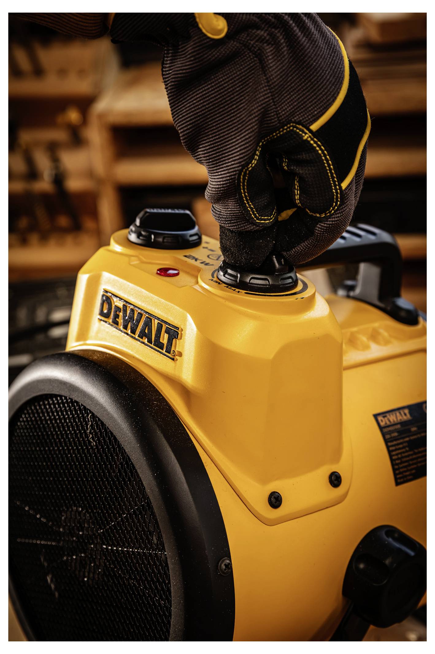 Behandschuhte Hand drückt auf die Steuerung eines gelben tragbaren DEWALT-Heizgeräts oder Ventilators mit großem schwarzem Gitter.