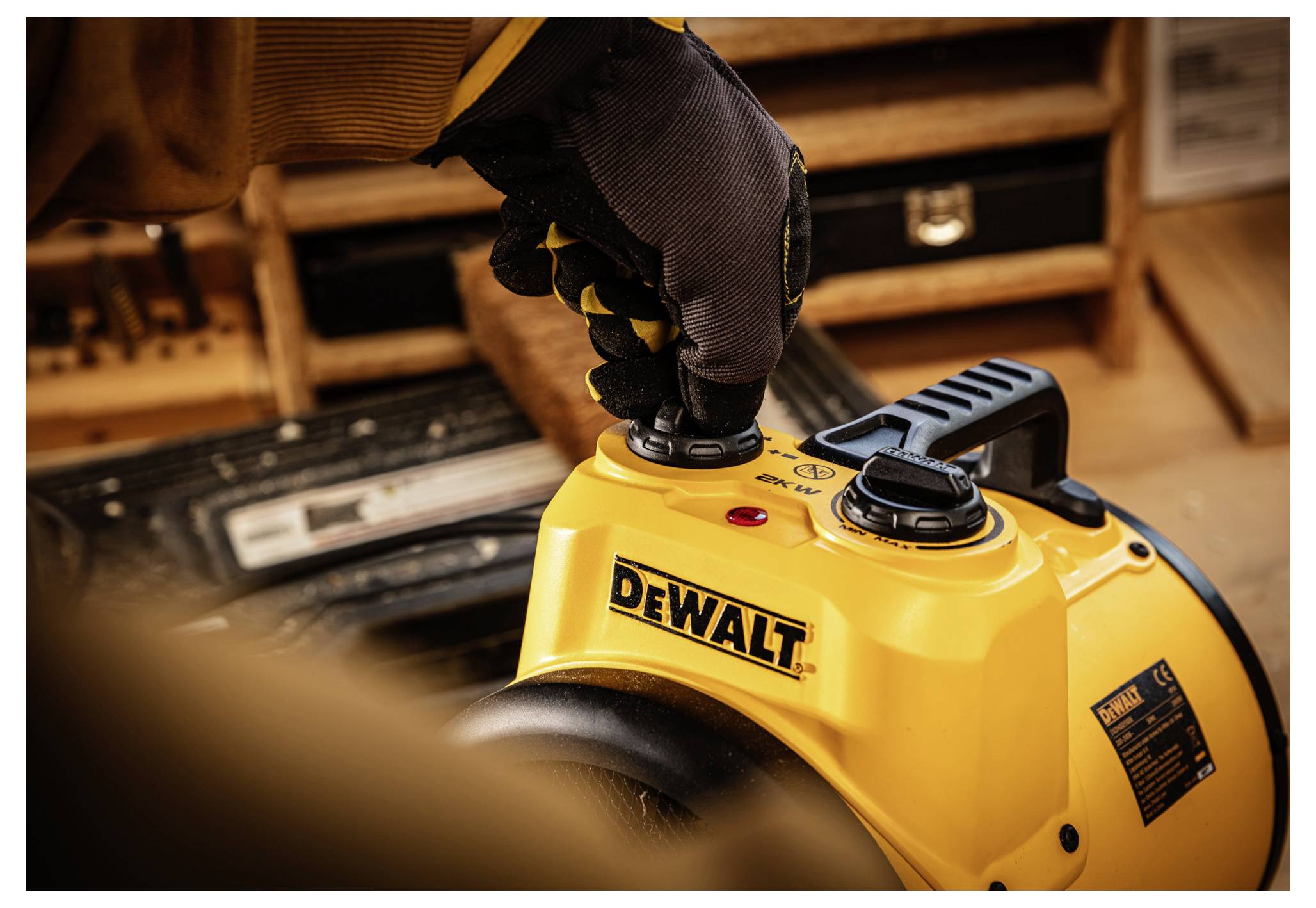 Behandschuhte Hand drückt den Steuerknopf auf einem gelben DEWALT-Elektrowerkzeug in einer Werkstatt.
