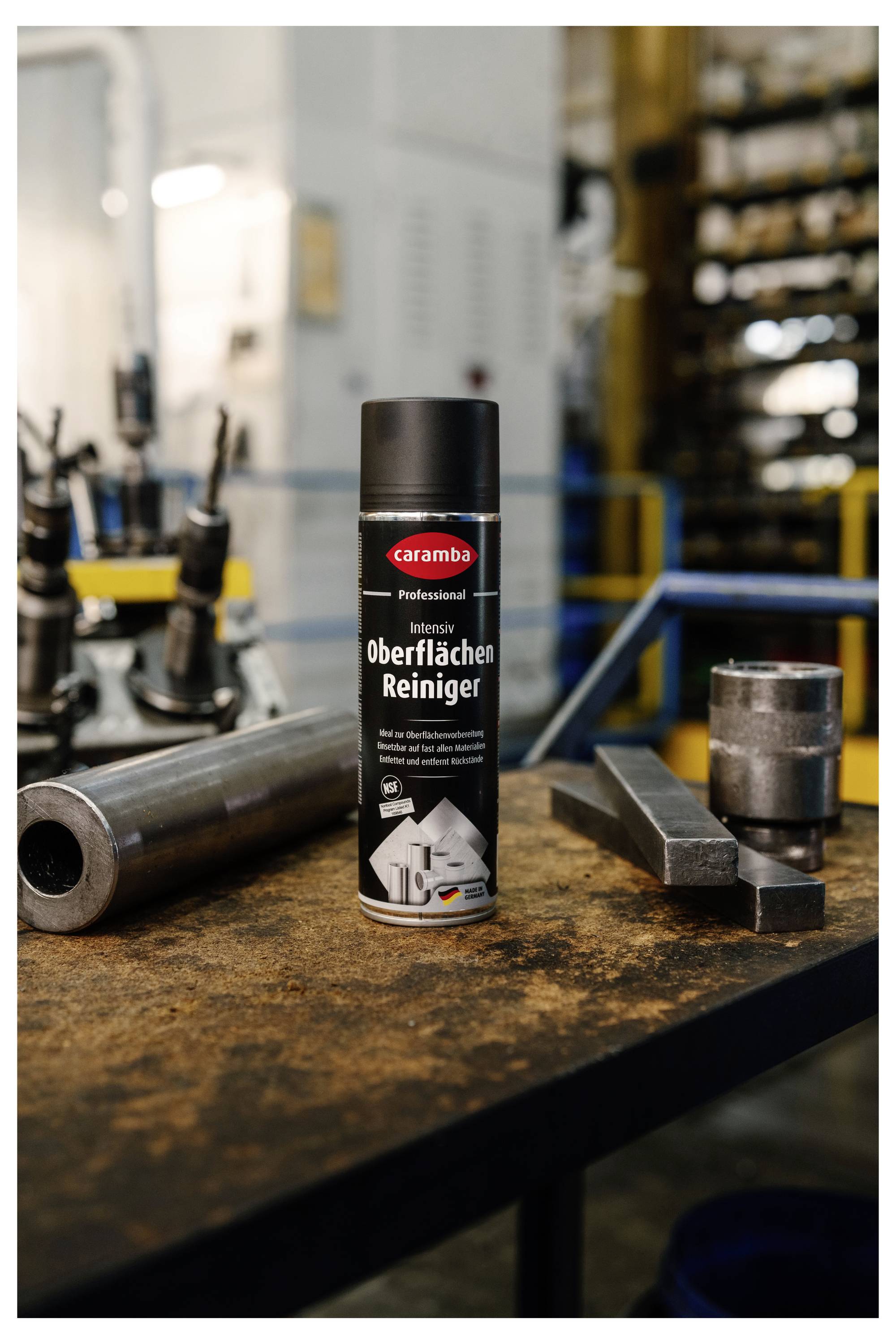 Eine Dose Caramba 'Intensiv Oberflächen Reiniger' steht auf einem Werkstatt-Tisch zwischen Metallwerkzeugen und Teilen in einer unscharfen industriellen Umgebung.