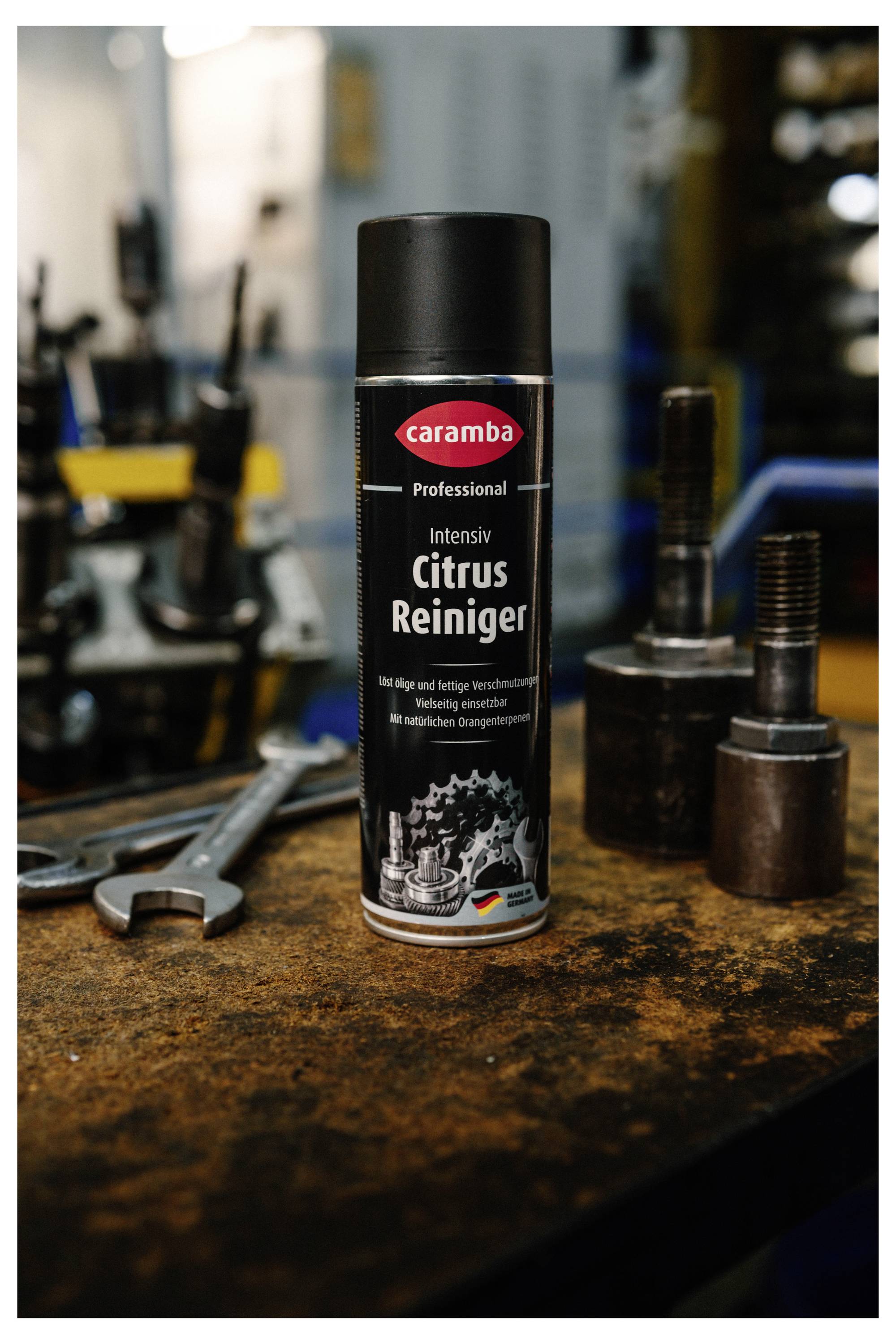 Eine Dose Caramba 'Intensiv Citrus Reiniger' Reiniger steht auf einer Werkbank neben einem Schraubenschlüssel und Metallteilen in einer Werkstatt.