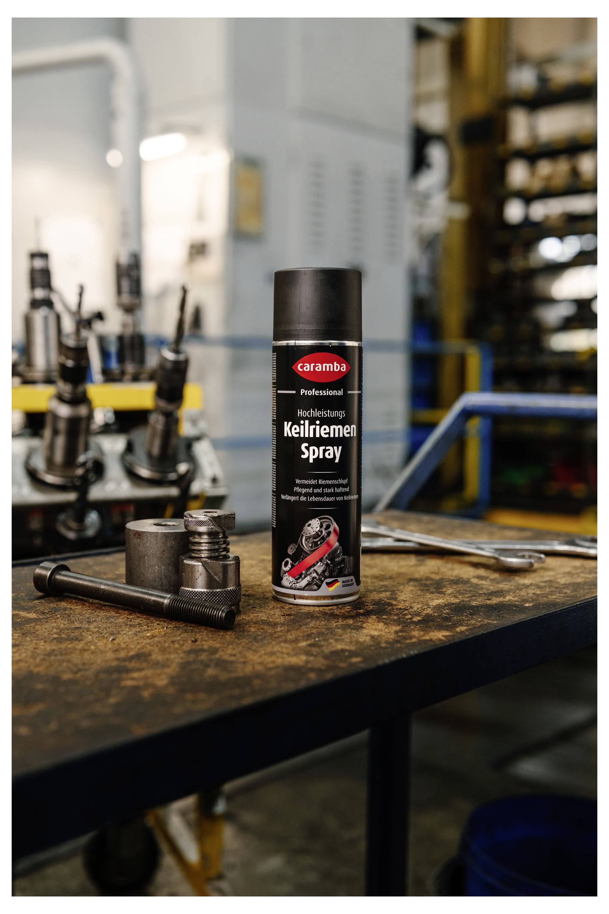 Eine Dose Caramba Professional Kettenreiniger-Spray steht auf einer Werkbank in einer Werkstatt, neben Metallwerkzeugen und Teilen.