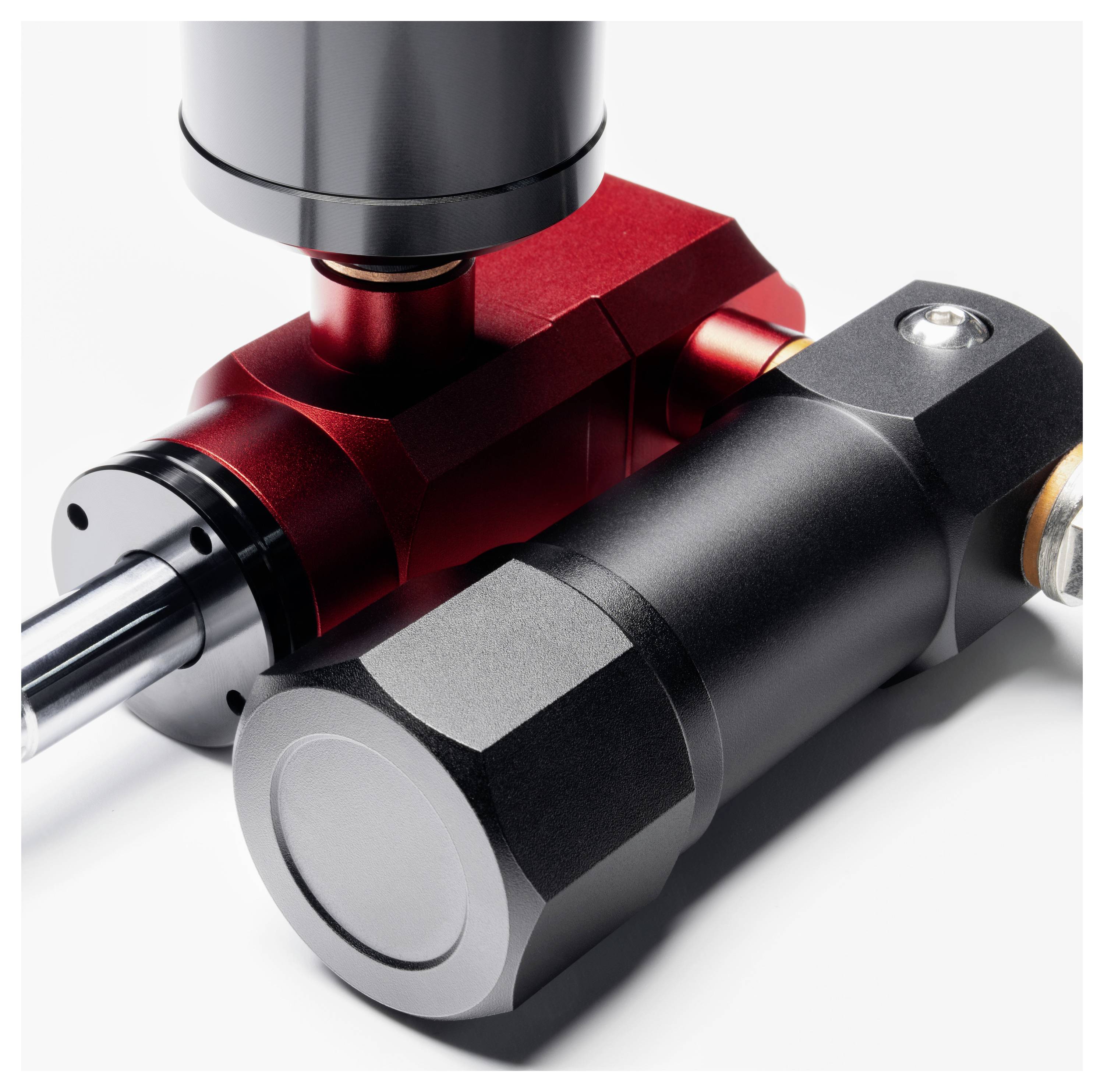 Nahaufnahme von zwei verbundenen metallischen hydraulischen oder pneumatischen Komponenten, eine rot und eine schwarz, mit einer silbernen Welle, die von links herausragt.