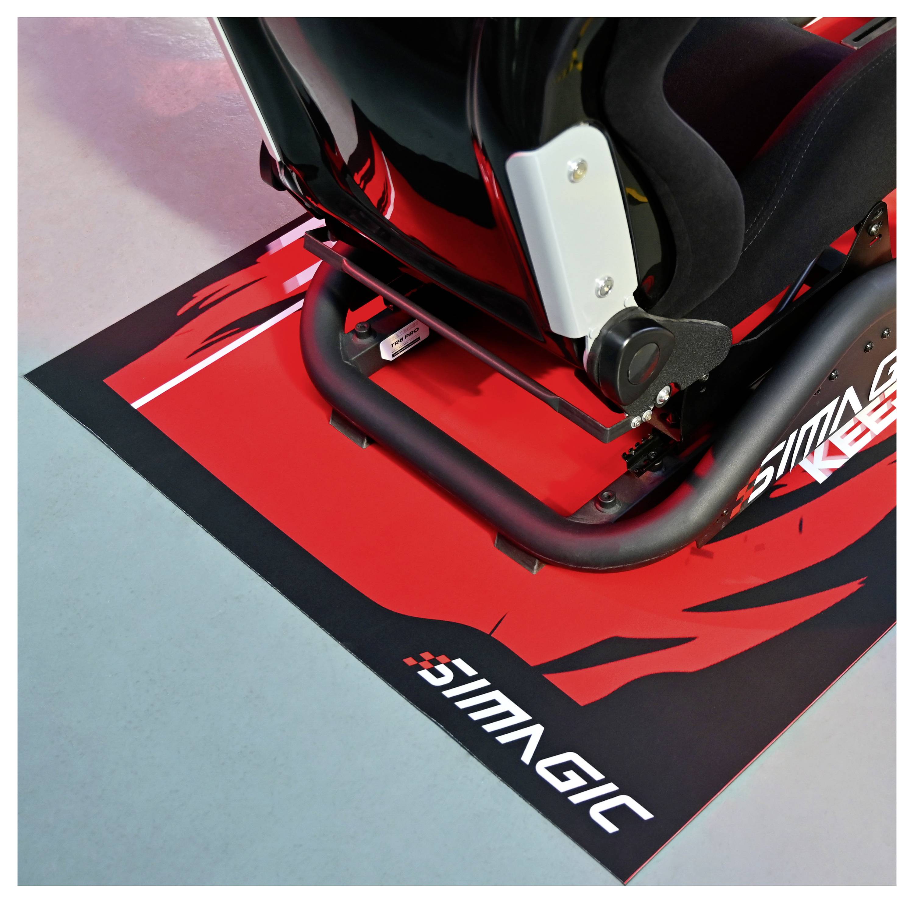 Nahaufnahme eines Racing-Simulator-Sitzes und einer Lenkbasis auf einer rot-schwarzen Matte mit der Marke „SIMAGIC