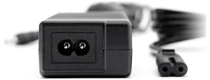 Schwarzer Wechselstrom-Netzadapter mit angebrachtem Kabel und zweipoliger Achter-Stecker auf weißer Oberfläche liegend.
