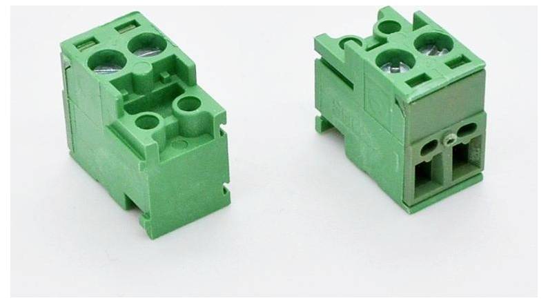 Zwei grüne Stromverteilerklemmen auf weißem Hintergrund, eine angewinkelt, um die Seite und Oberseite zu zeigen, die andere von vorne.