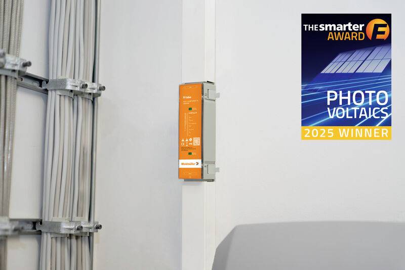 An der Wand montierte orangefarbene elektrische Komponente neben Kabelkanälen, mit einem Aufkleber „The smarter E AWARD