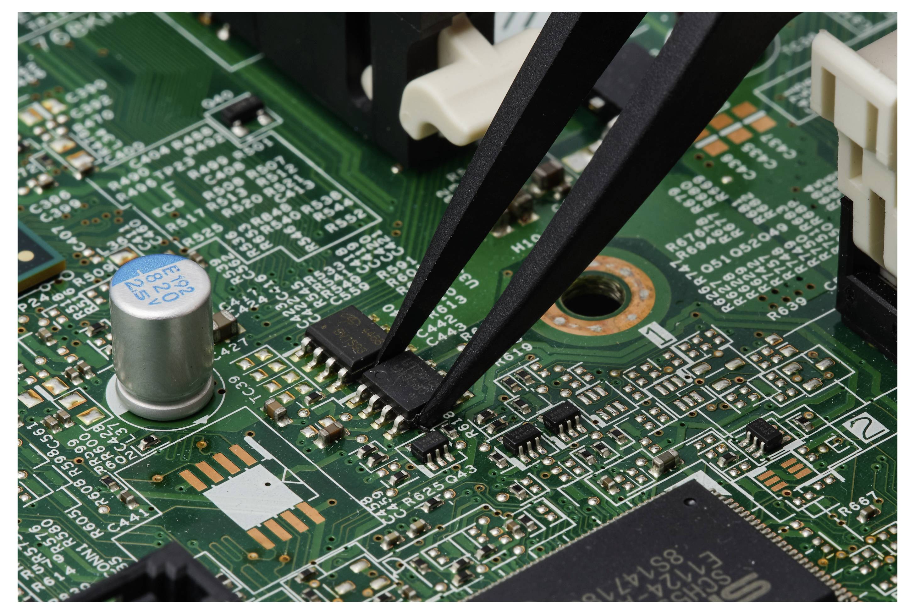 Pinzetten platzieren einen winzigen oberflächenmontierten Chip auf einer grünen Leiterplatte während der Elektronikfertigung.