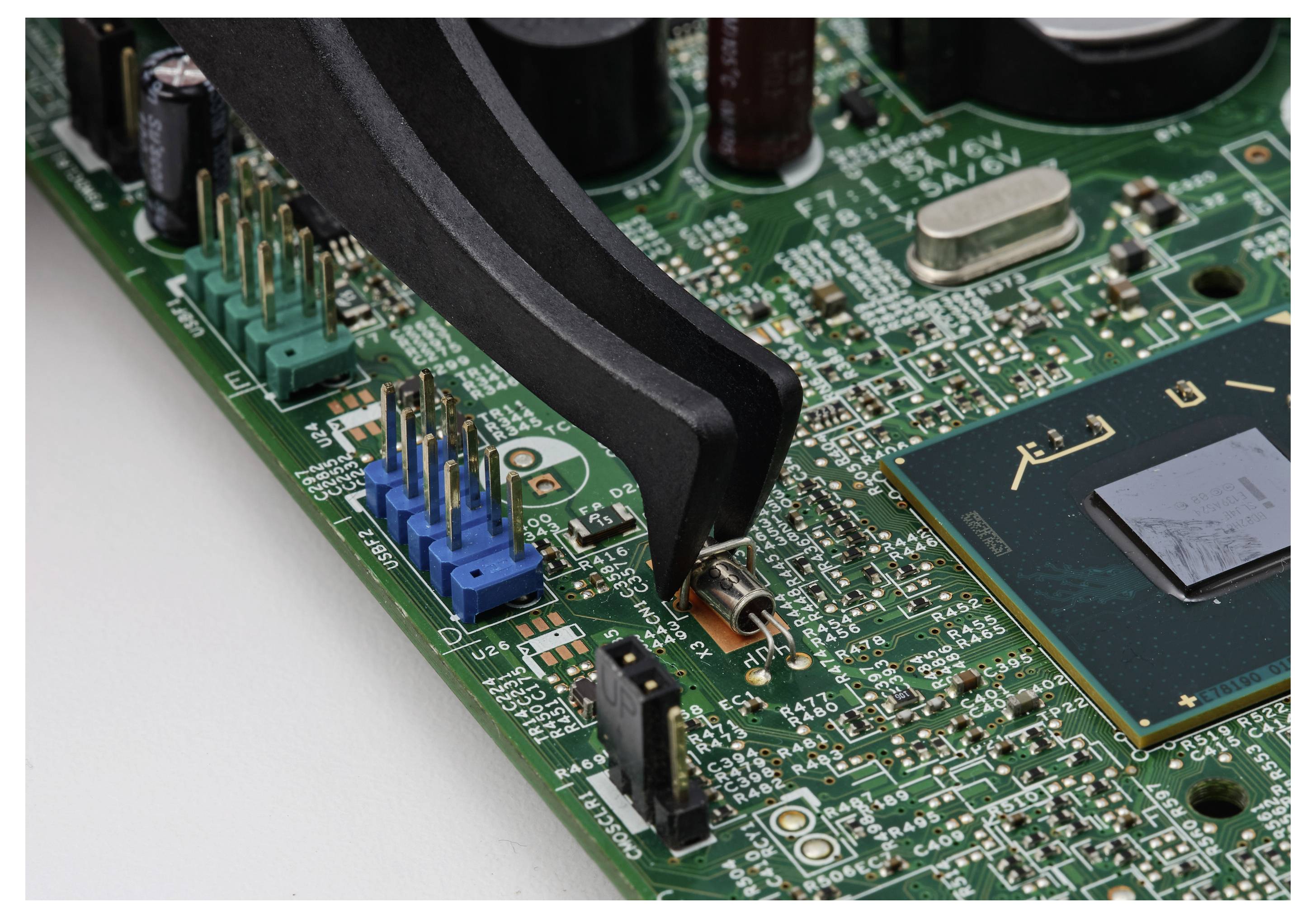 Nahaufnahme einer Computerschaltplatine mit einem Chip, Anschlüssen und Testleitungen, die für Reparatur oder Diagnose auf Komponenten geklemmt sind.