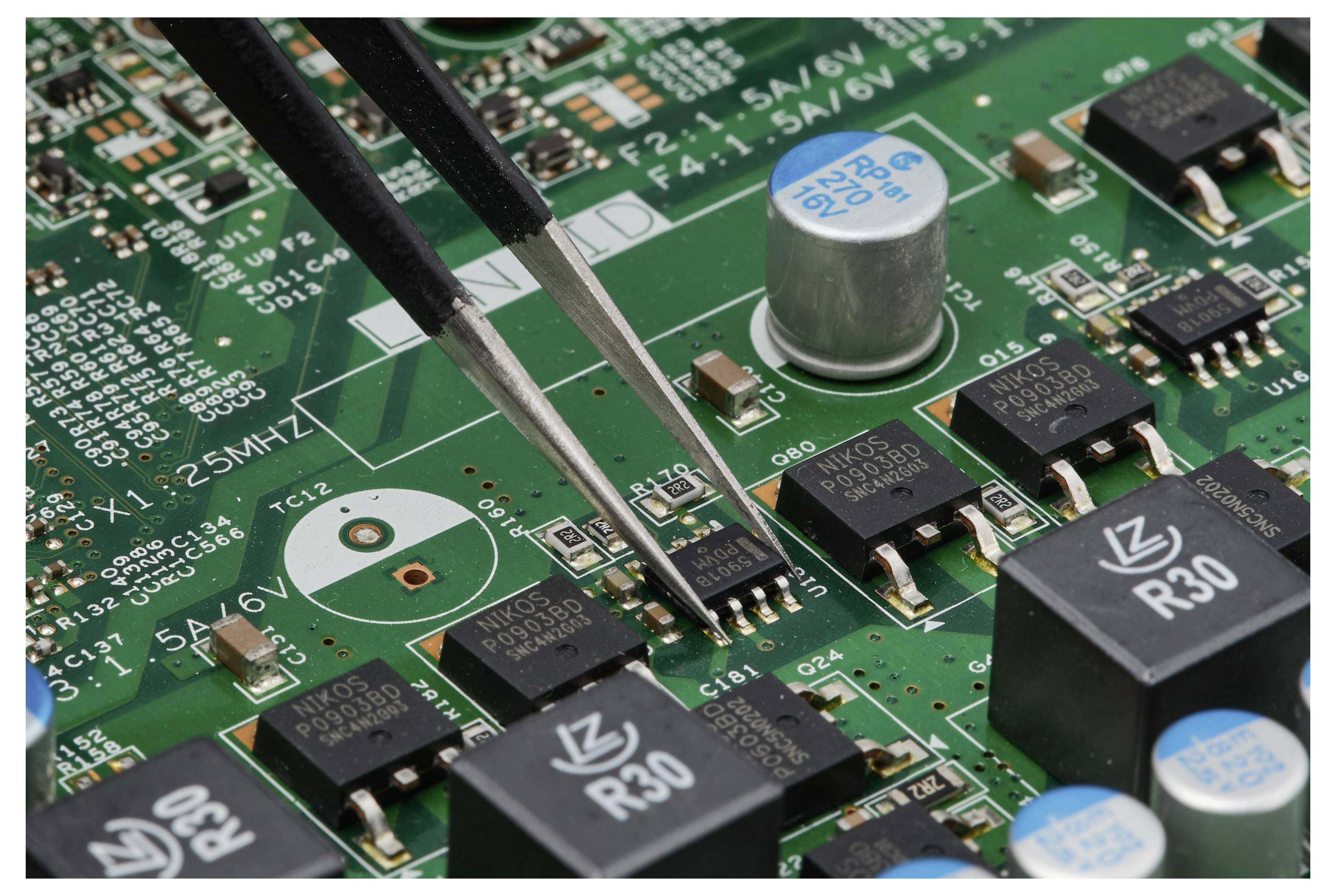 Eine Pinzette platziert einen winzigen oberflächenmontierten Chip auf einer grünen Leiterplatte während der Elektronikbaugruppe.