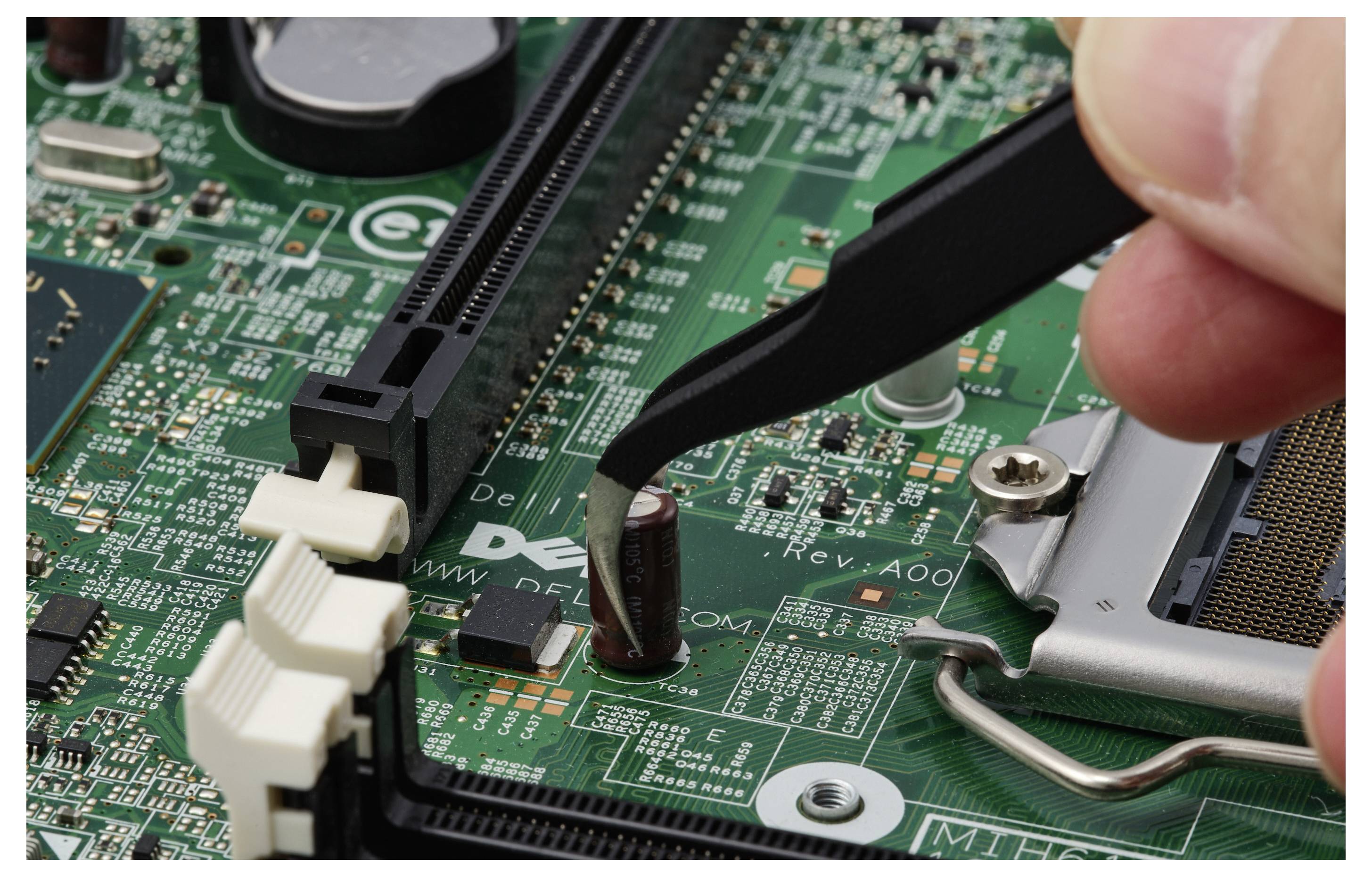 Nahaufnahme einer Pinzette und eines Fingers, die einen Kondensator auf einer Computerplatine in der Nähe des CPU-Sockels einbauen.