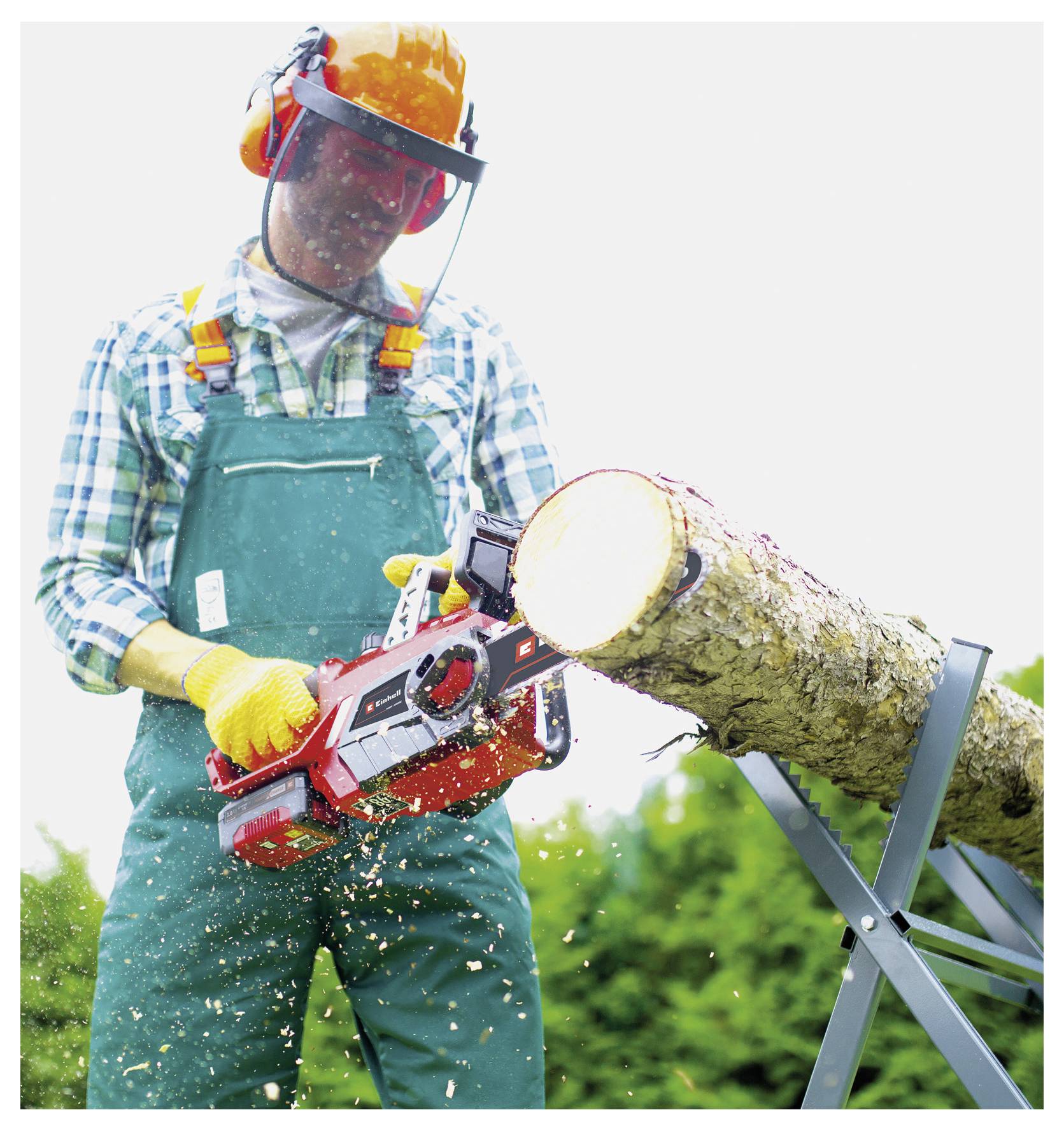 Person in Schutzausrüstung benutzt eine Kettensäge, um einen Baumstamm auf einem Metallständer im Freien zu schneiden, wobei Holzspäne herumfliegen.