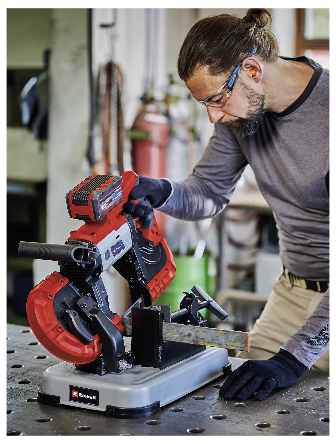 Man in safety glasses using a red miter saw to cut metal in a workshop.