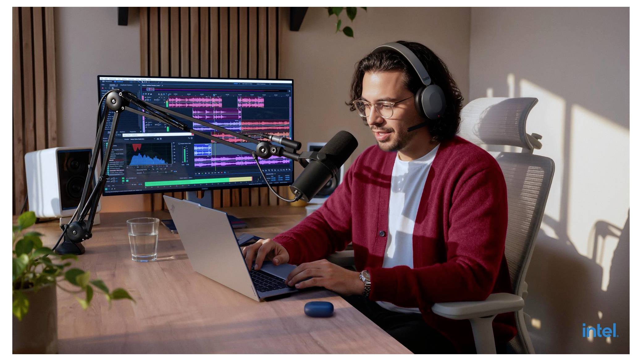 Ein Mann mit Kopfhörern nimmt Audio auf oder bearbeitet Audio auf einem Laptop an einem Schreibtisch mit Mikrofon und zwei Monitoren in einem Heimstudio.