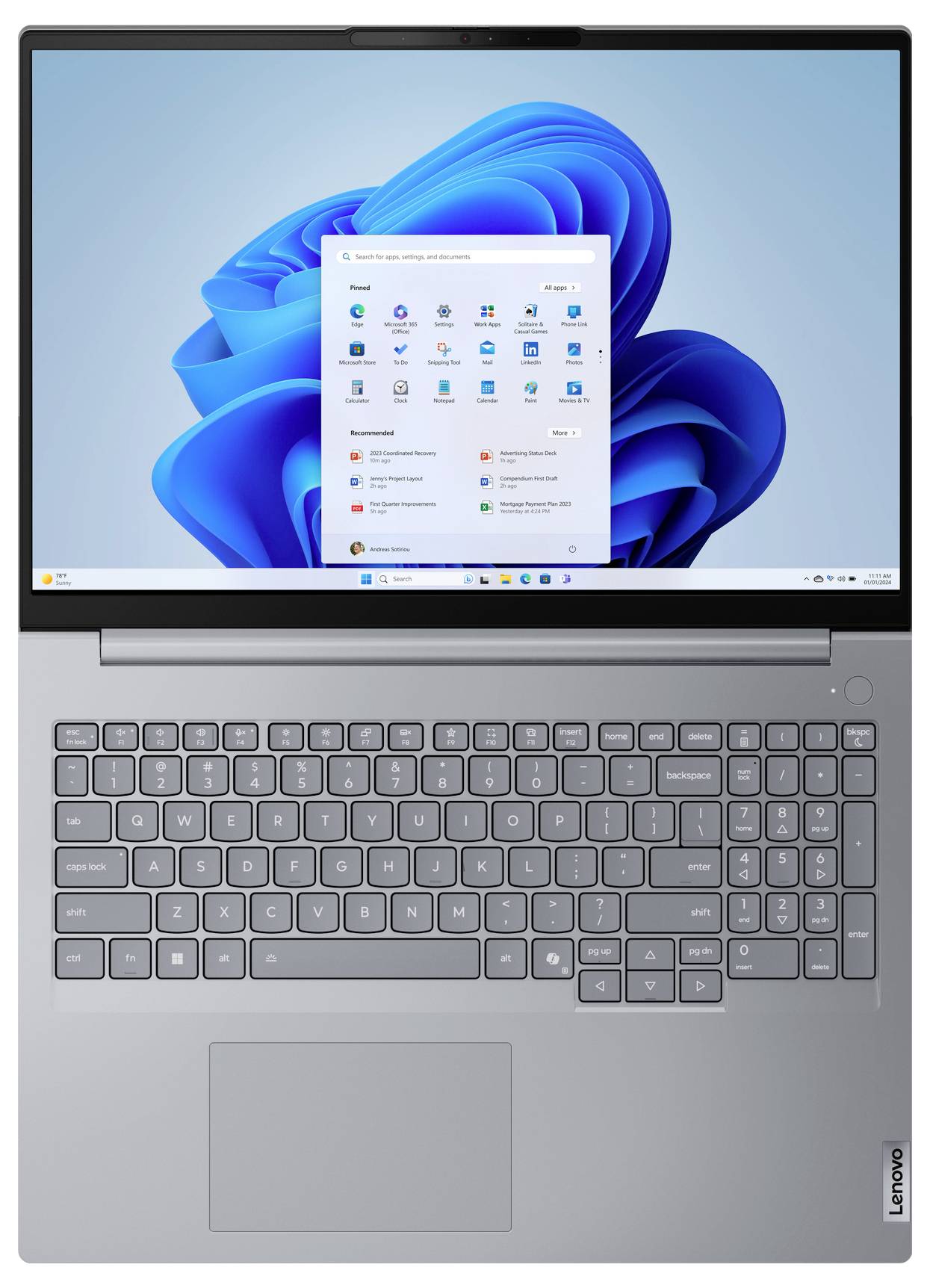 Silberner Lenovo-Laptop offen mit Windows 11-Desktop und Startmenü auf dem Bildschirm, zeigt Tastatur und Trackpad.