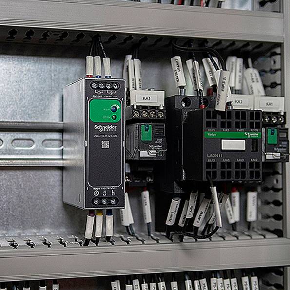Schaltschrank mit mehreren Schneider-Electric-Steuergeräten und verdrahteten Relais/Schützen auf Hutschiene.