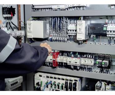Techniker inspiziert ein elektrisches Bedienfeld mit Verkabelung, Relais, Leistungsschaltern und Komponenten der Industrieautomation.