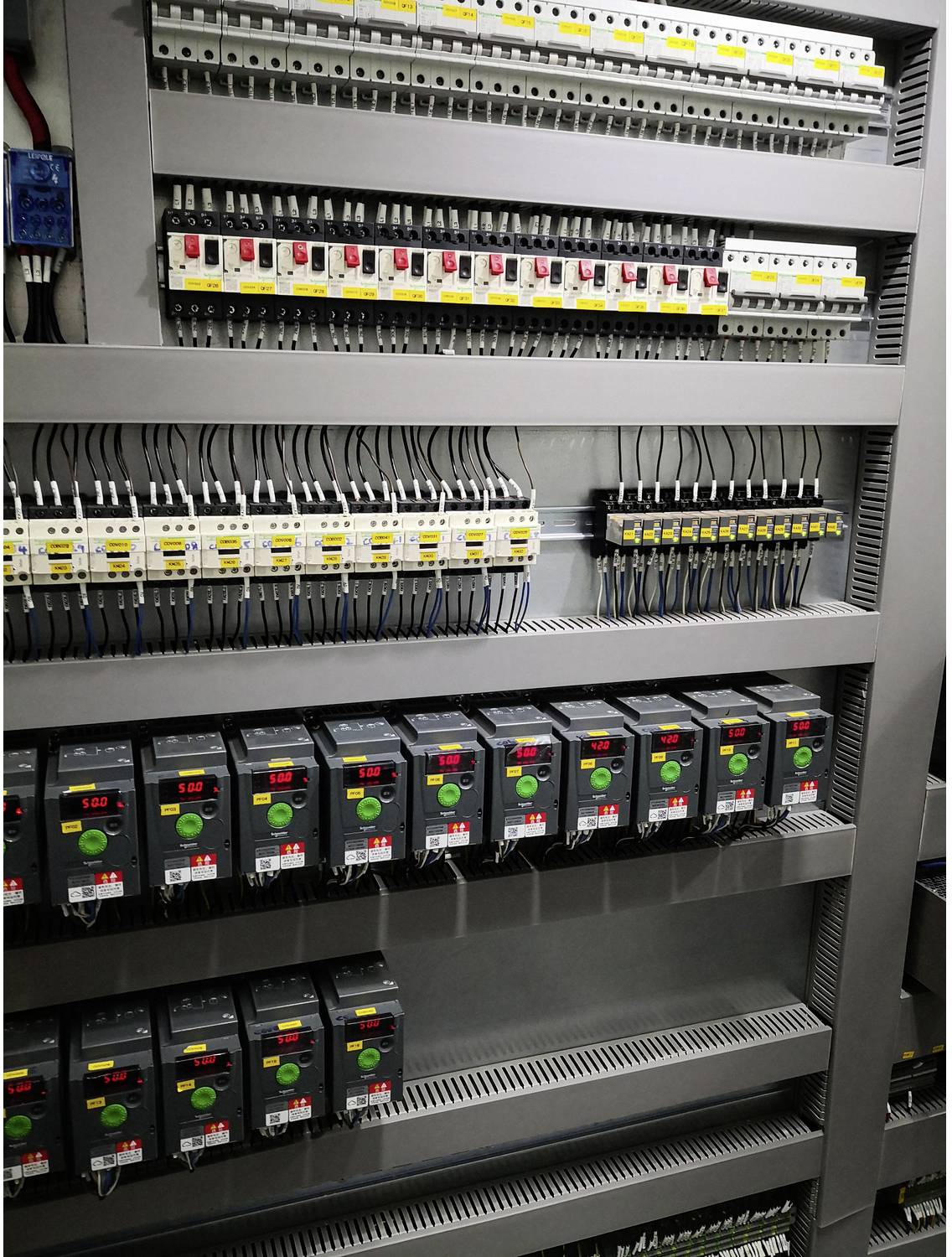 Elektrischer Schaltschrank mit Reihen von Leistungsschaltern, Relais und Motorantrieben auf DIN-Schienen montiert, zeigt organisierte Industrieverdrahtung und Stromregelungen.