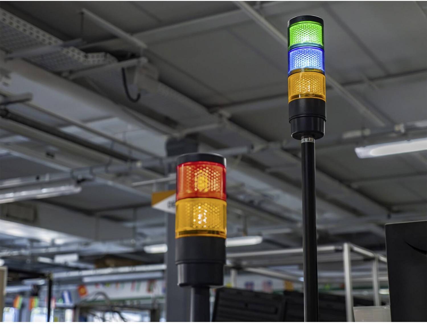 Zwei Industriesignaltürme in einer Fabrik oder einem Lagerhaus, einer mit roten und orangefarbenen Leuchten, der andere mit grünen, blauen und orangefarbenen Leuchten.