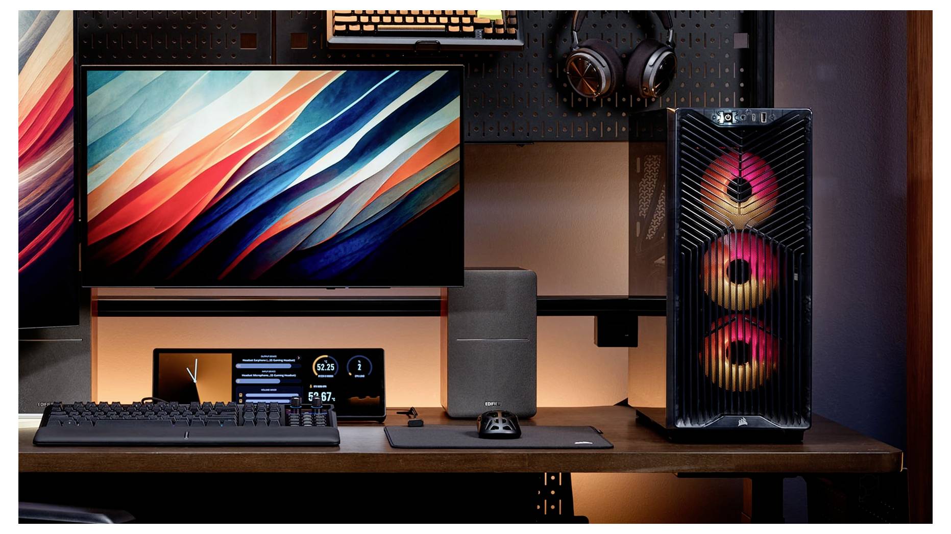 Gaming-Schreibtischaufbau mit Monitor, Tastatur, Maus, Kopfhörer und beleuchtetem Tower-PC auf einem Holzschreibtisch.