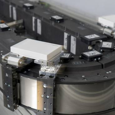 Nahaufnahme eines automatisierten Laborinstruments mit einem rotierenden kreisförmigen Probenkarussell und einem montierten Sensor- oder Lesekopf, der mehrere kleine Tabletts verarbeitet.