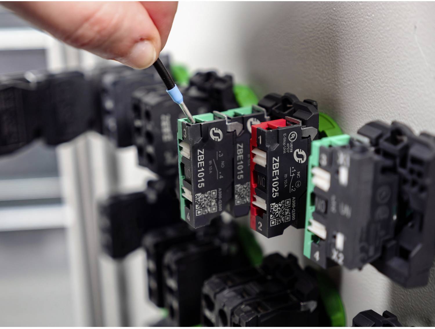 Eine Hand benutzt einen Schraubendreher, um eine Reihe von industriellen elektrischen Klemmleisten auf einem Steuerpaneel zu justieren.