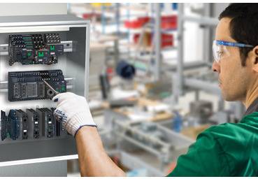 Techniker mit Schutzbrille und Handschuhen inspiziert und justiert elektrische Steuerungskomponenten in einem geöffneten Industrieschrank in einer Fabrik.