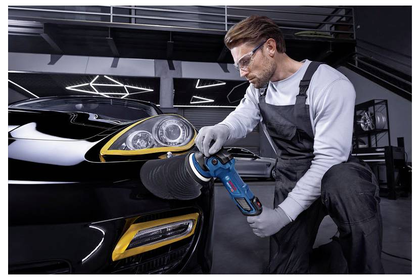 Ein Mechaniker poliert das vordere Scheinwerfer eines schwarzen Sportwagens in einer Werkstatt mit einem tragbaren Poliergerät.