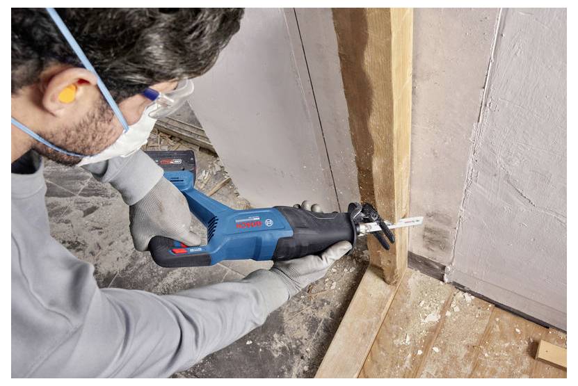 Person, die eine blaue Bosch-Stichsäge verwendet, um einen Holzständer während einer Hausrenovierung zu schneiden, trägt Handschuhe, Schutzbrille und eine Maske.